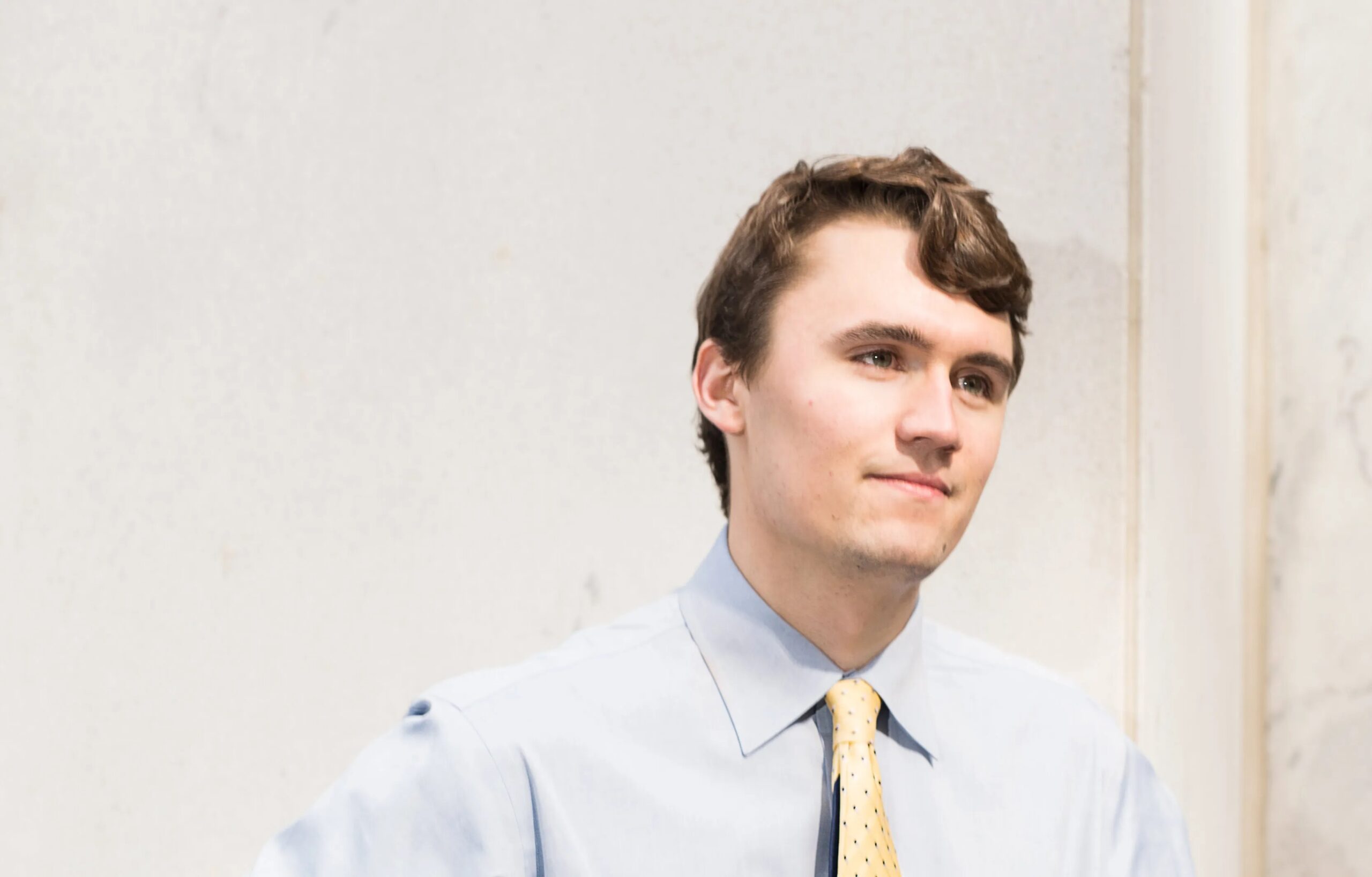 18 Year old Charlies Kirk – Tumisang Bogwasi Young Charlie Kirk wearing a light blue shirt and yellow tie, standing against a light-colored wall with a composed expression.