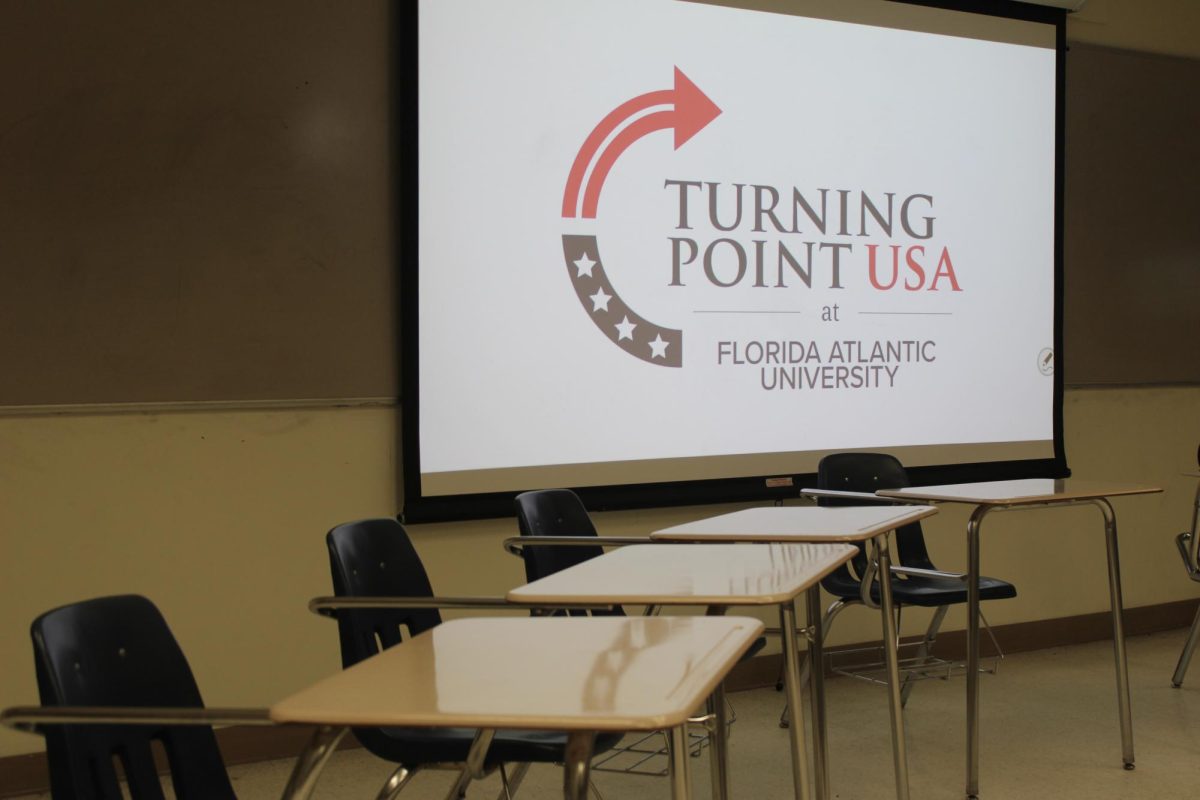 Turning Point USA Engages Students at Florida Atlantic University – Tumisang Bogwasi Classroom with empty desks facing a projection screen showing the Turning Point USA logo and “Florida Atlantic University” chapter name.