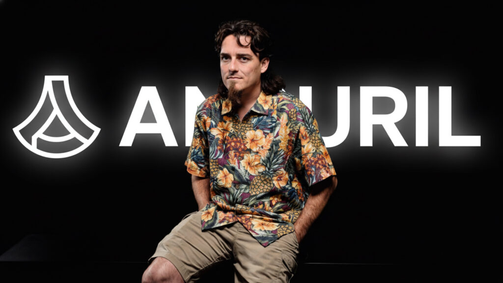 Palmer Luckey The Maverick Behind Anduril copy – Tumisang Bogwasi Palmer Luckey wearing a colorful floral shirt and cargo shorts, seated in front of a glowing Anduril logo on a black background.