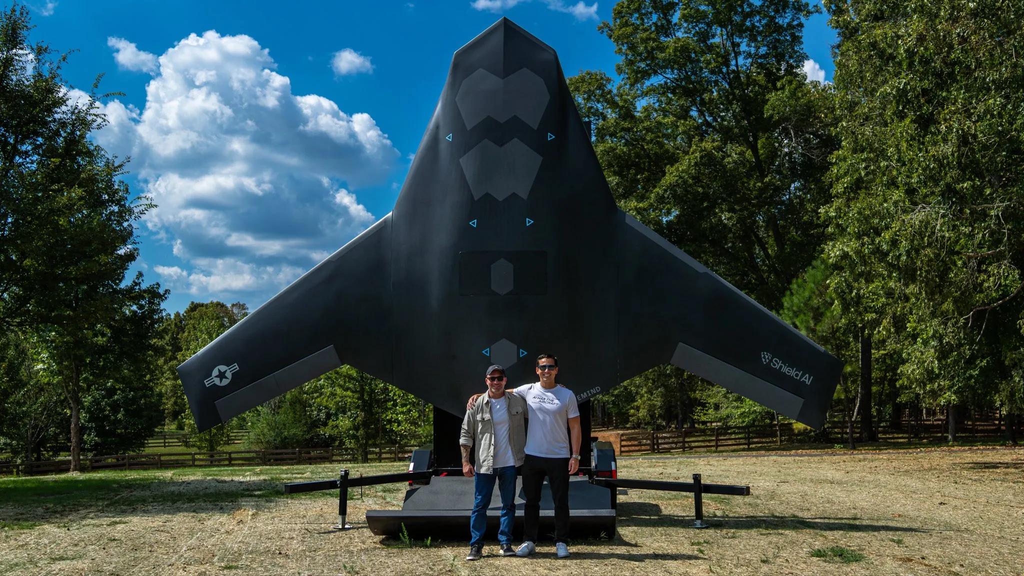 Ryan Tseng and Team Member with the X-Bat Prototype – Tumisang Bogwasi Ryan Tseng of Shield AI and an unidentified team member standing in front of the X-Bat VTOL aircraft in a field under a bright blue sky.