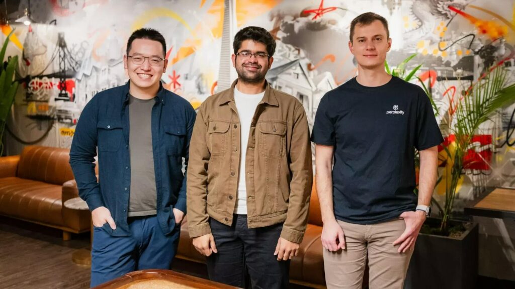 The Founding Trio of Perplexity AI – Tumisang Bogwasi Founders of Perplexity AI — Johnny Ho, Aravind Srinivas, and Denis Yarats — standing together in front of a colorful mural in a modern office lounge.