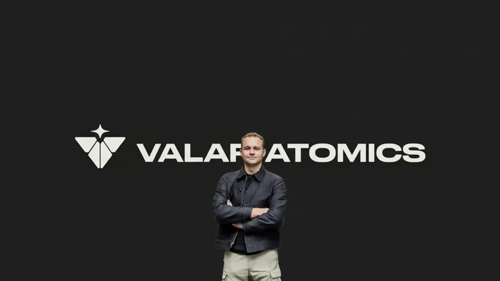 Isaiah Taylor Founder of Valar Atomics – Tumisang Bogwasi Isaiah Taylor standing in front of the Valar Atomics logo on a dark background with arms crossed.