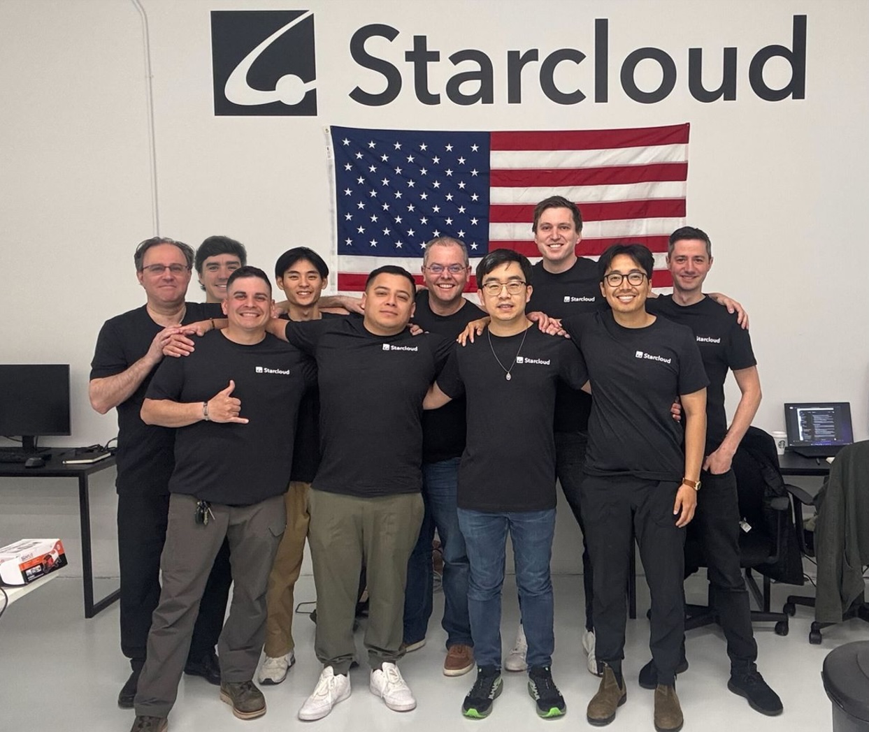 The StarCloud Team at Mission Control – Tumisang Bogwasi StarCloud team posing for a group photo in front of an American flag and company logo inside their workspace.