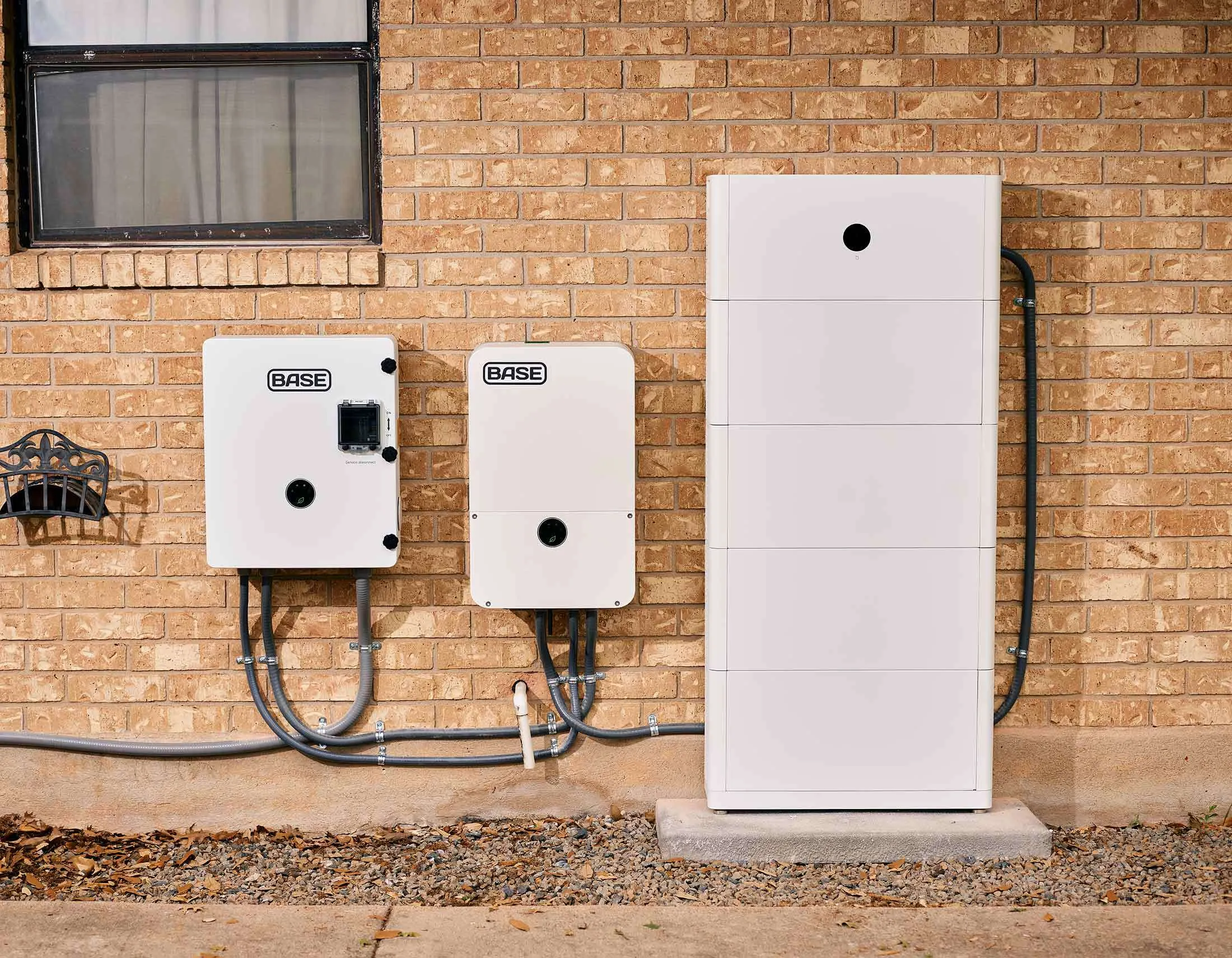 Base Home Energy System Installation – Tumisang Bogwasi Exterior wall-mounted Base energy system components installed beside a residential building, including inverter units and a tall battery cabinet.