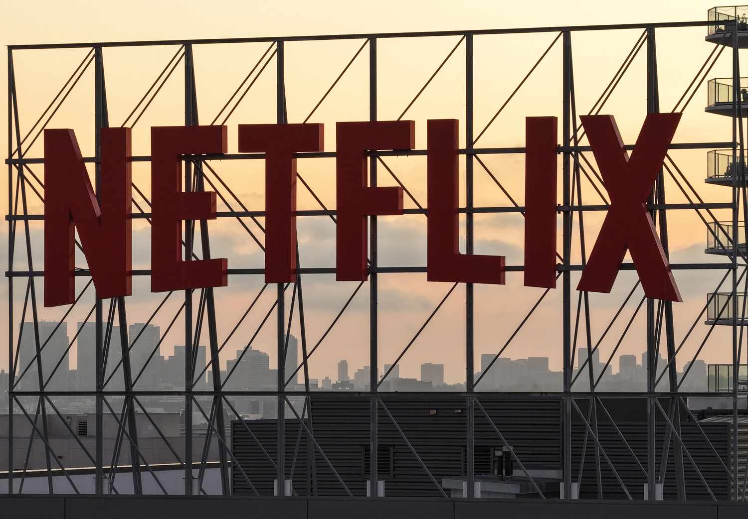 Netflix Skyline Billboard at Sunset – Tumisang Bogwasi Large red Netflix billboard structure silhouetted against a city skyline at sunset.
