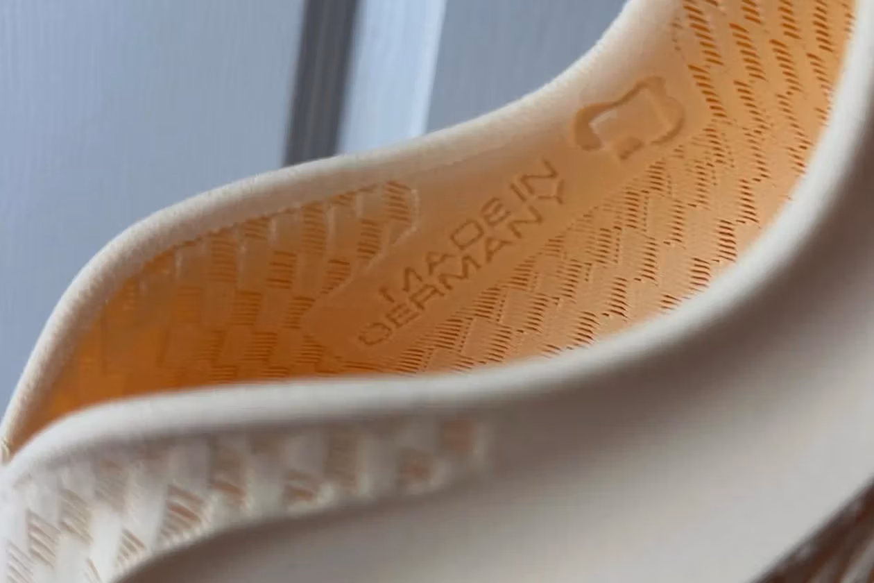 Close-up of a hand holding a modern Nike running shoe featuring a knit upper and sculpted sole against a blurred urban background.