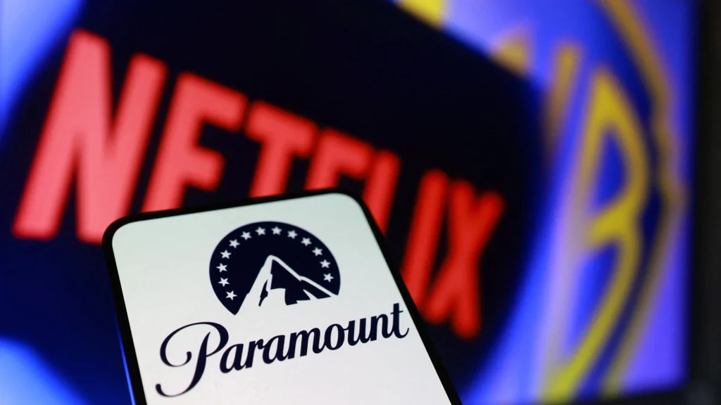 Paramount and Netflix Logos in a Media Industry Context – Tumisang Bogwasi A mobile phone displaying the Paramount logo in front of blurred Netflix and Warner Bros. logos on a screen.