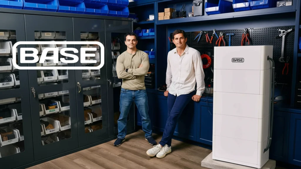 Zach Dell and Justin Lopas Co-Founders of Base Power in Their Hardware Lab – Tumisang Bogwasi Zach Dell and Justin Lopas, co-founders of Base Power, standing in a blue workshop next to a BASE energy unit and wall of tools.