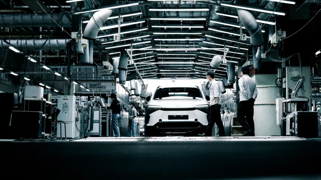 Factory workers and a white electric vehicle in a high-tech automotive production line