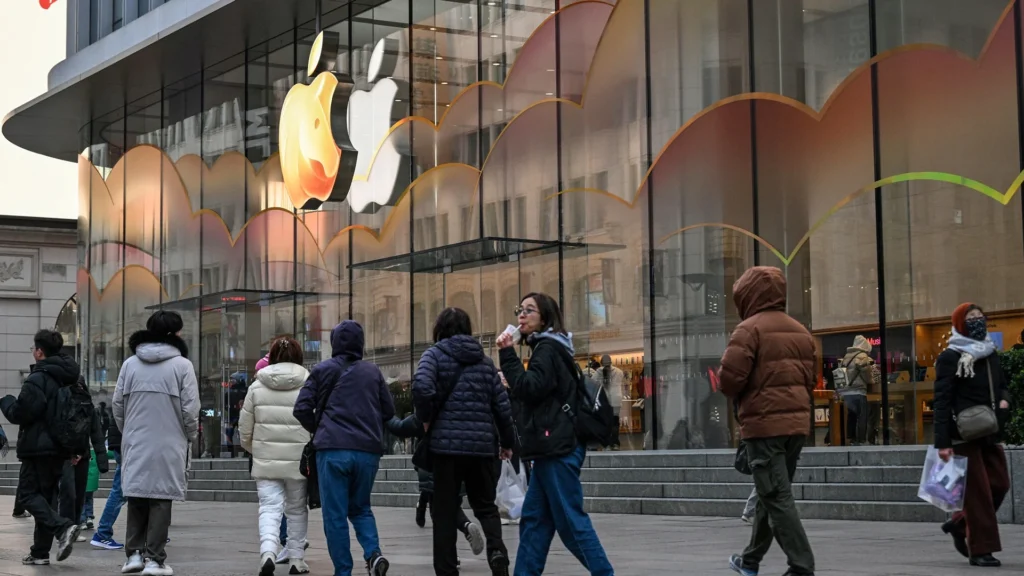 Apple Store as a Global Consumer Landmark – Tumisang Bogwasi People walking outside a large glass-front Apple Store with a glowing Apple logo, viewed from street level in a busy city setting.