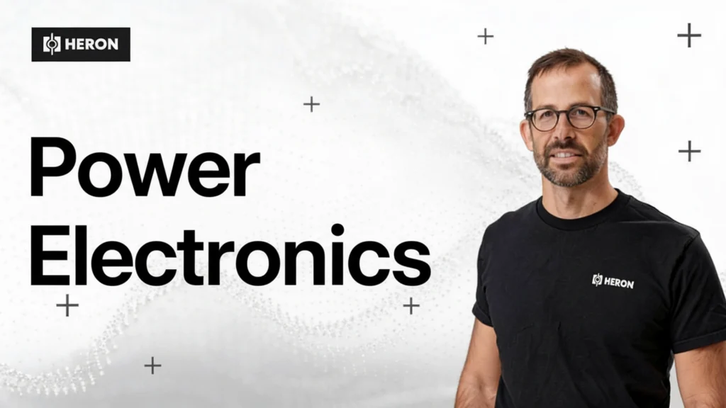 Drew Baglino wearing glasses and a black Heron T-shirt standing next to large text reading “Power Electronics” with the Heron logo displayed above.