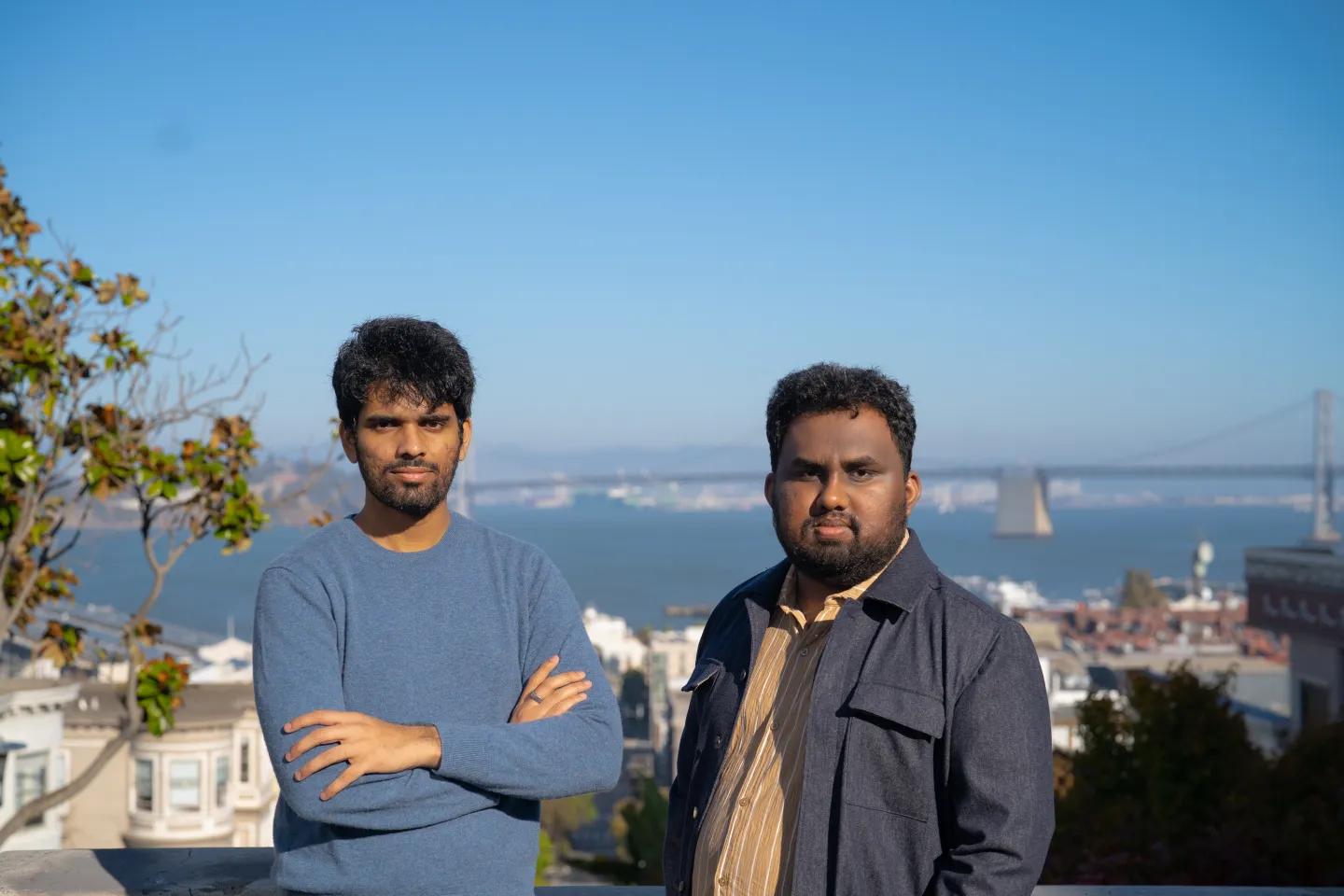 Esha-and-Varunjpg – Tumisang Bogwasi Two men, identified as Giga.ai co-founders Esha and Varun, standing outdoors with a city and bridge in the background.