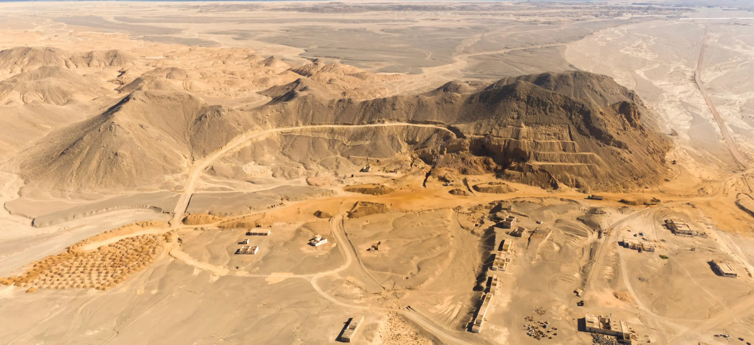 Legacy Geological Exploration Site in Desert Terrain – Tumisang Bogwasi Aerial view of a desert mountain with terraced excavation roads and small exploration structures scattered across the arid terrain.