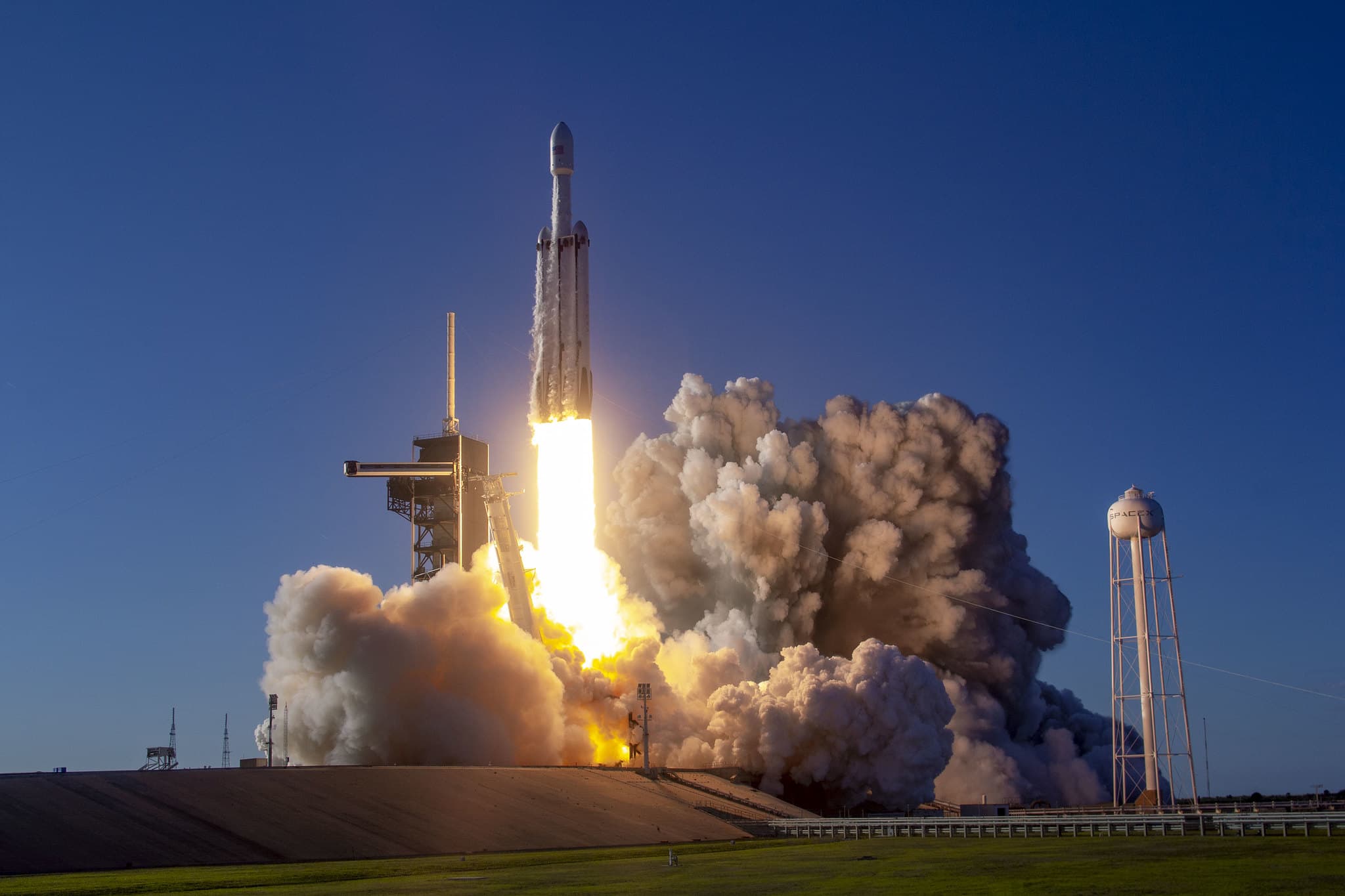 Rocket Launch Liftoff with Plume and Launch Tower – Tumisang Bogwasi Rocket launching from a pad with bright exhaust flame and thick smoke plume under a clear blue sky.