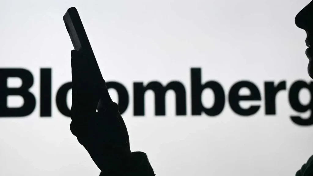 Silhouette of a person holding a smartphone in front of a Bloomberg logo display.