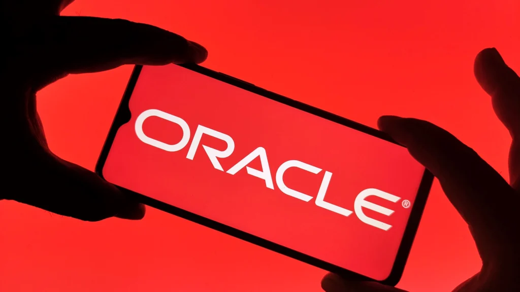 Oracle Logo Displayed on Smartphone Screen – Tumisang Bogwasi Hands holding a smartphone showing the Oracle logo on a red screen.