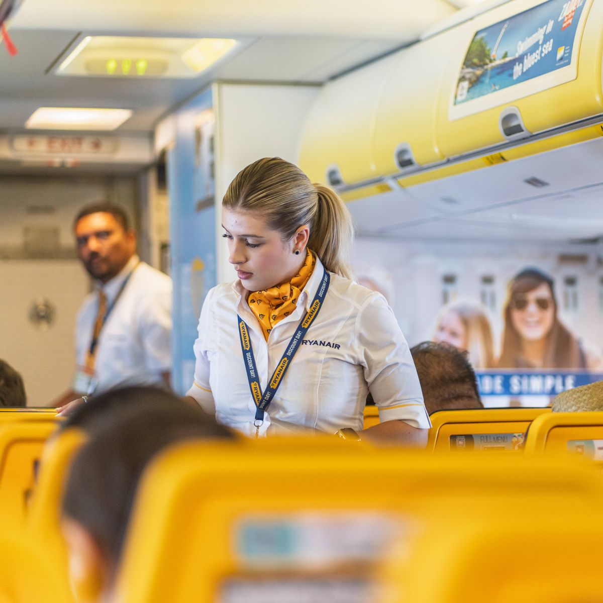 Ryanair cabin crew member walking through the aircraft cabin while assisting passengers before takeoff.