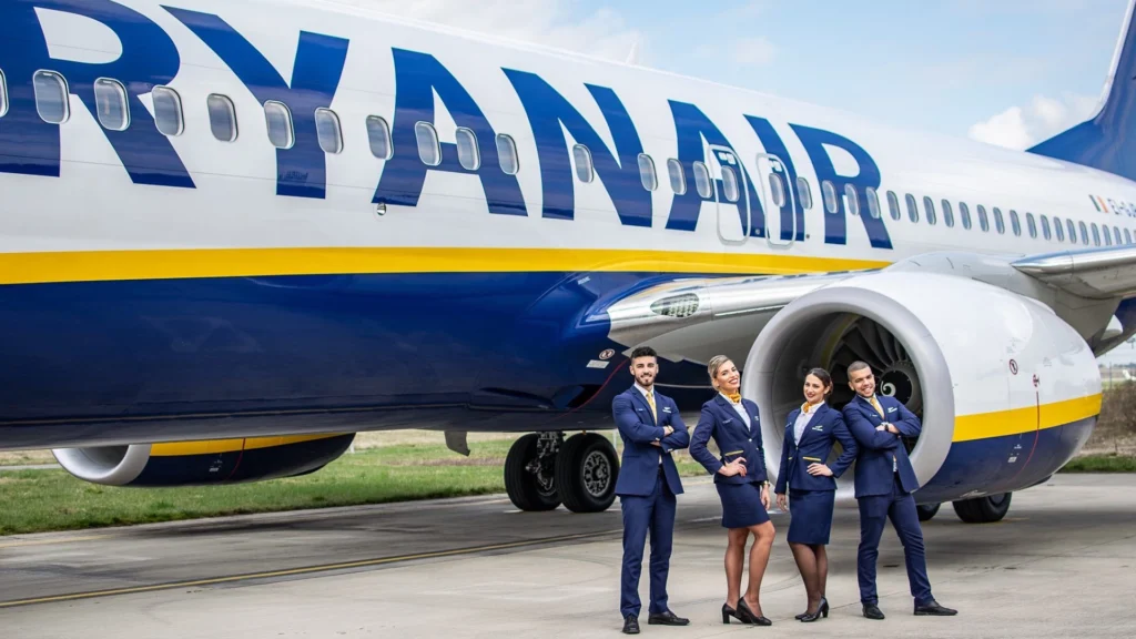Four Ryanair cabin crew members standing beside a Ryanair passenger aircraft on the airport tarmac.