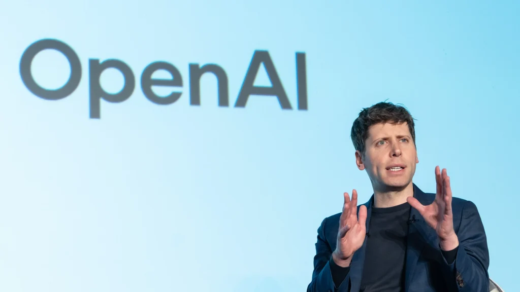 Sam Altman Speaking Under the OpenAI Banner – Tumisang Bogwasi Sam Altman speaking on stage with the OpenAI logo displayed behind him.