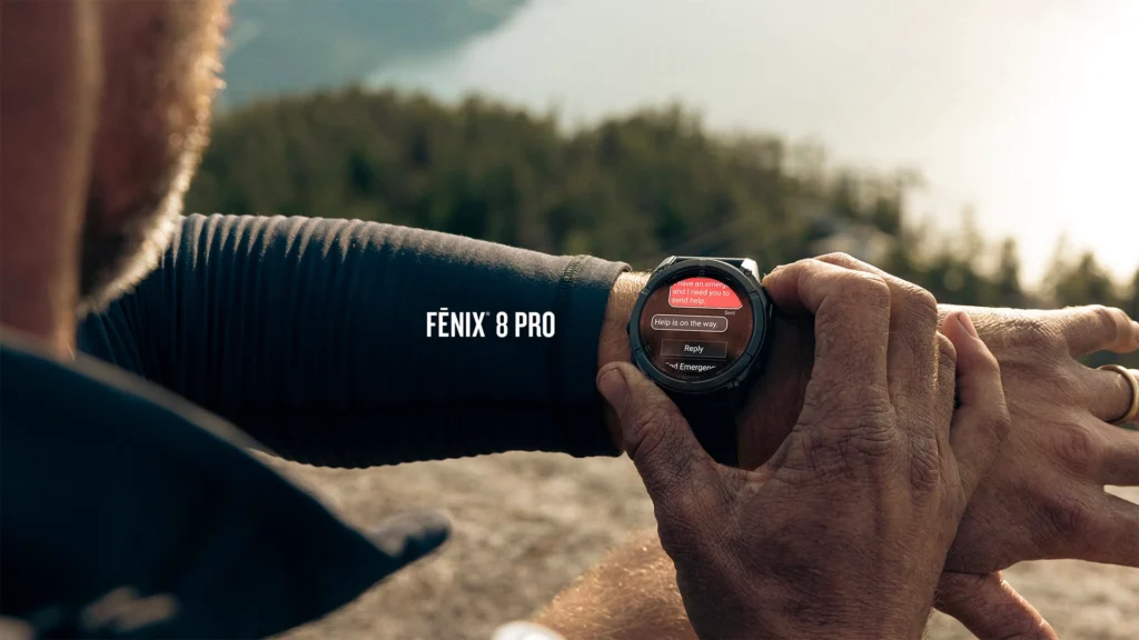 Close-up of a person using a Garmin Fēnix 8 Pro smartwatch outdoors, displaying an emergency message conversation on the watch screen.