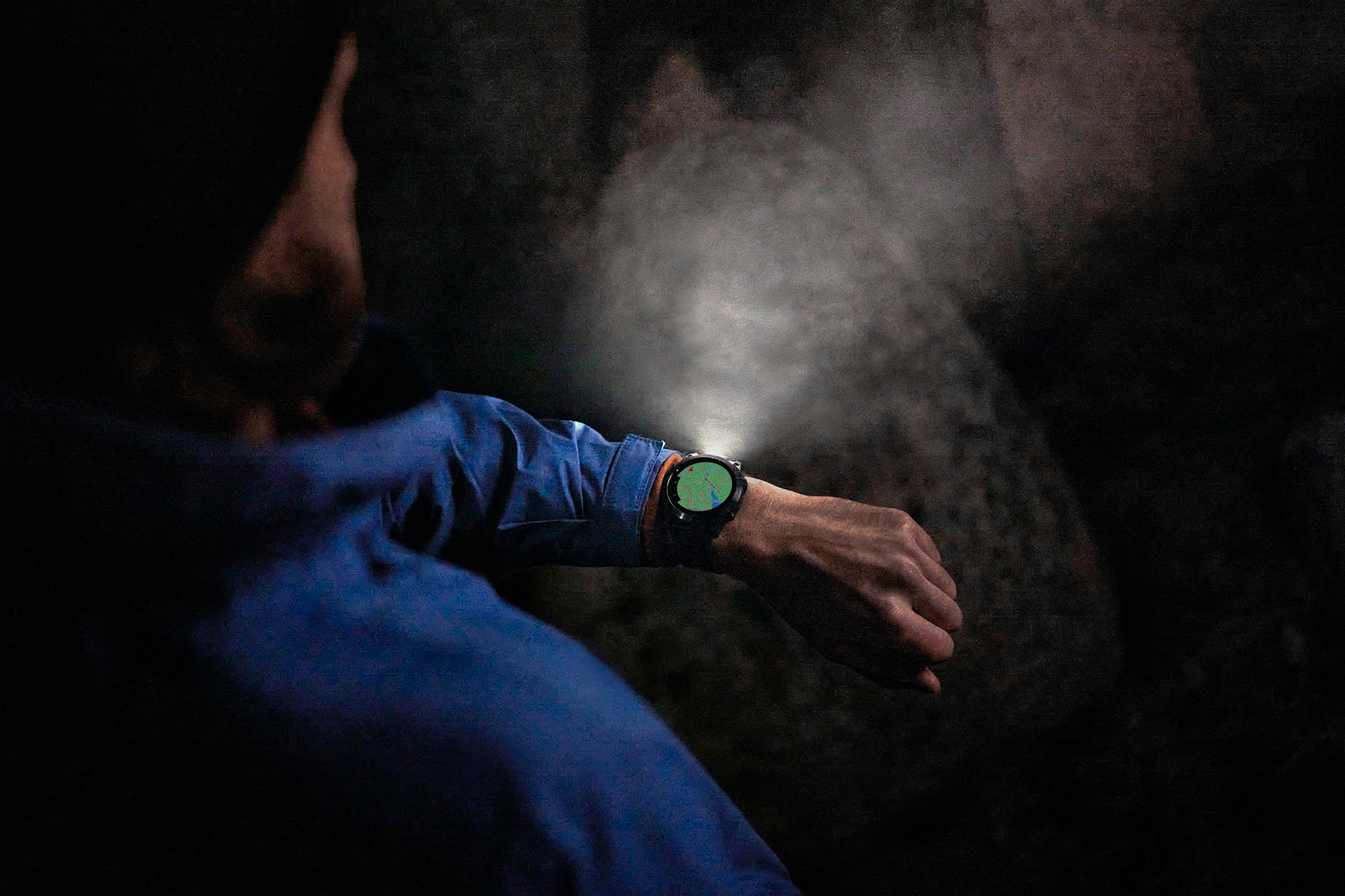Person wearing a Garmin smartwatch in a dark outdoor setting, with the watch displaying a map and emitting light from its integrated flashlight feature.