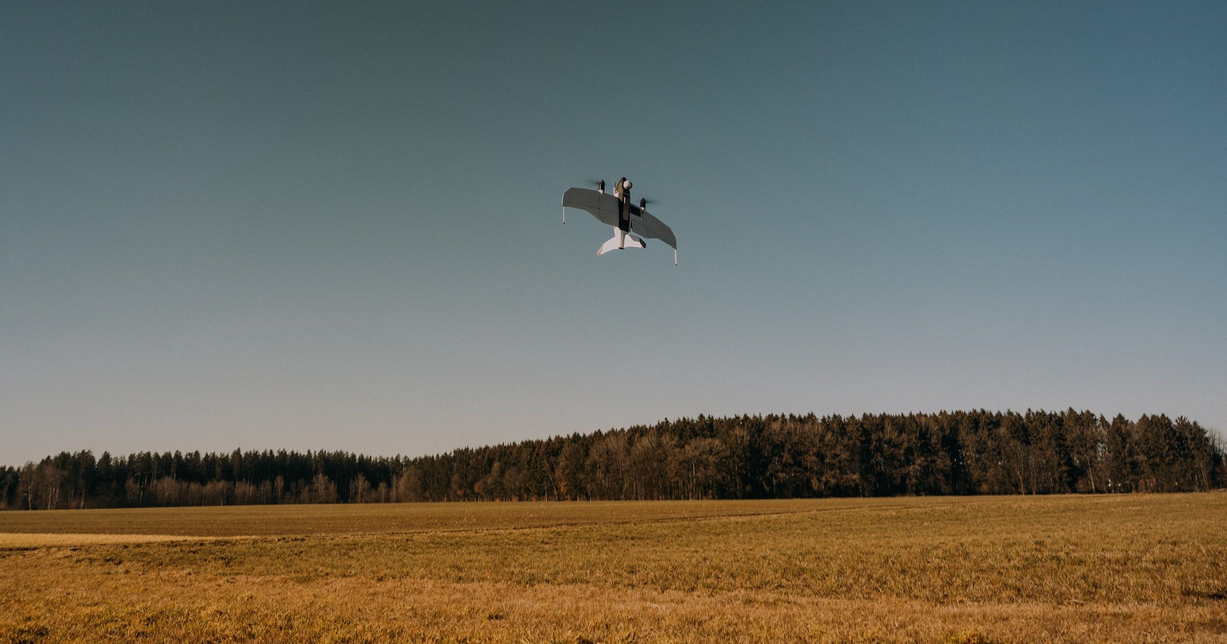 Quantum Systems Drone Conducting Autonomous Flight Operations – Tumisang Bogwasi Quantum Systems fixed-wing drone flying over an open field with a forested horizon in the background during a test or operational mission.