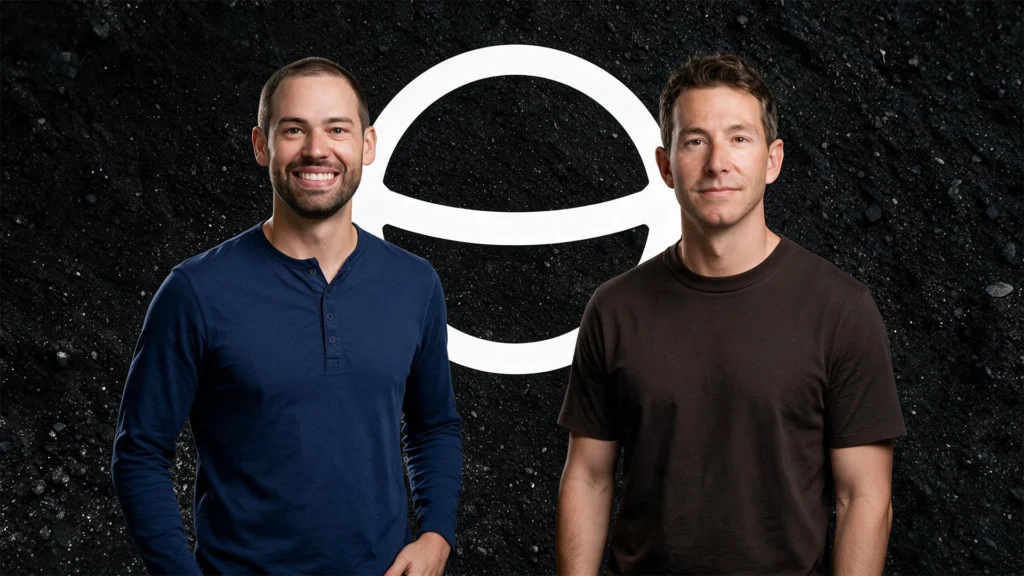 Two smiling men stand side by side in casual shirts, posed against a dark, gravel-like background with a large white circular logo between them.