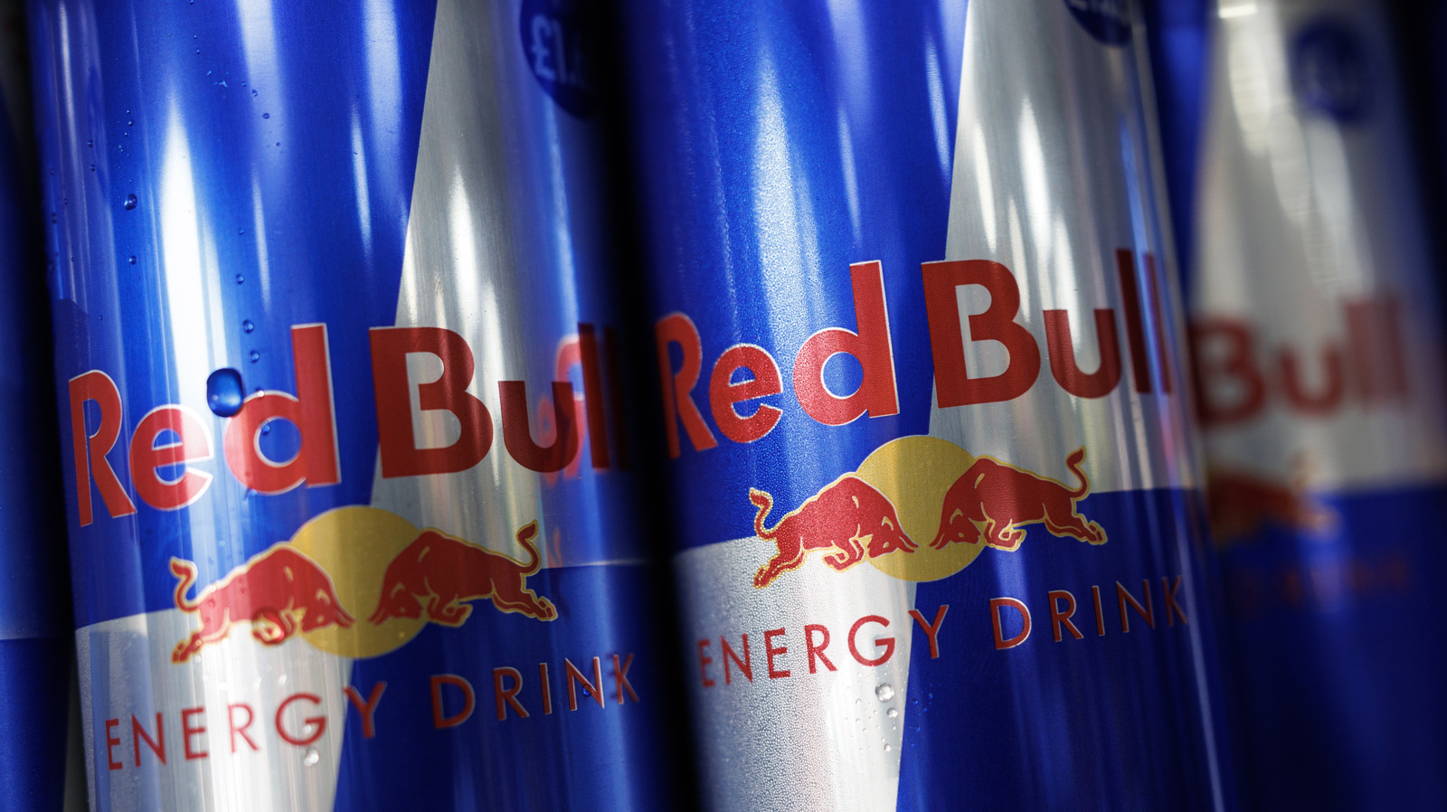 Red Bull Energy Drinks Displayed on Retail Shelf – Tumisang Bogwasi Several cans of Red Bull Energy Drink lined up on a retail shelf with the brand's signature blue and silver design prominently visible.