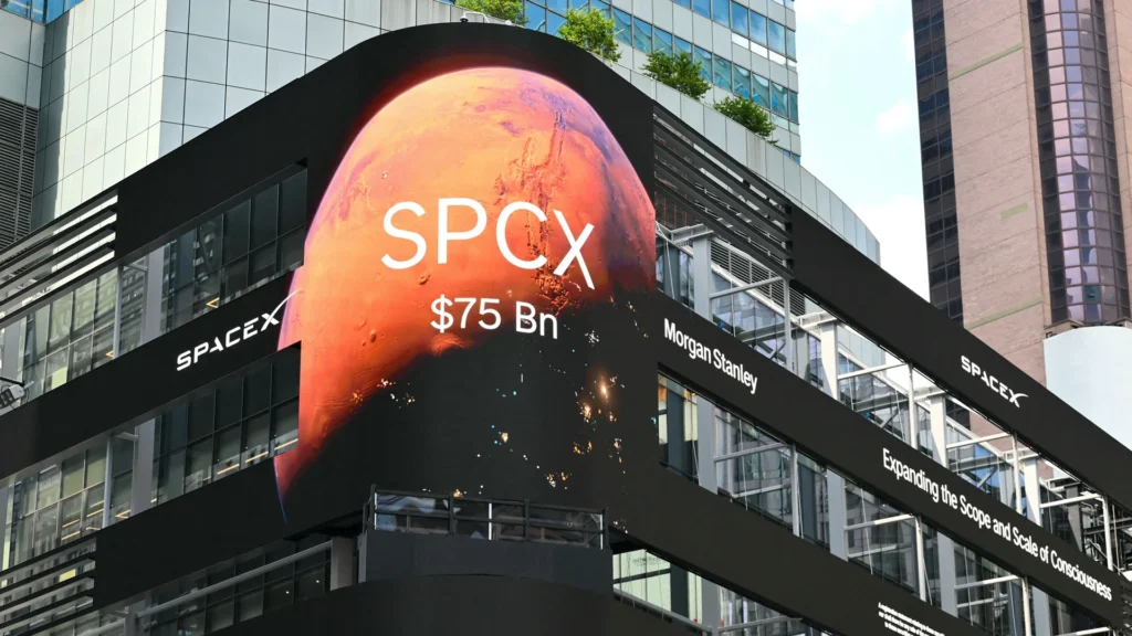 Large outdoor digital billboard displaying SpaceX's SPCX listing with a Mars-themed background, a $75 billion valuation, and Morgan Stanley branding on a modern city building.