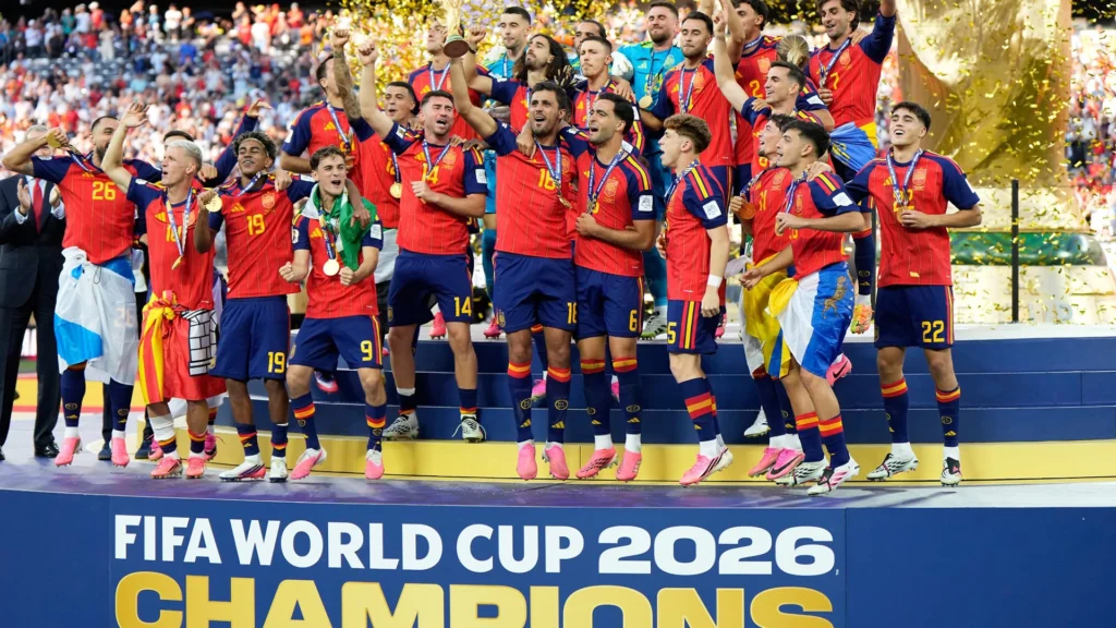 Spain Celebrates Victory at the 2026 FIFA World Cup – Tumisang Bogwasi Spain's men's national football team celebrates on the podium after winning the 2026 FIFA World Cup, holding the trophy as gold confetti falls around them.