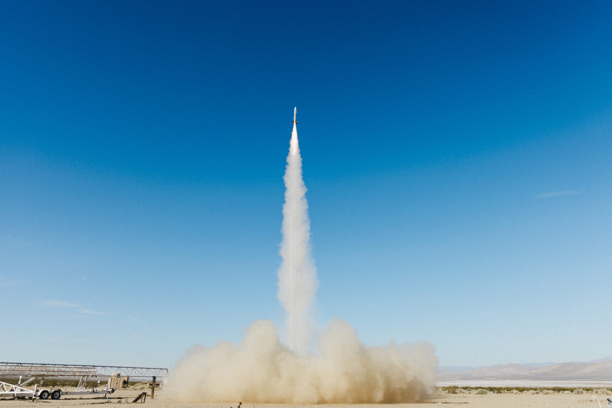A Castelion test rocket climbing on a smoke trail into a clear blue sky above the desert